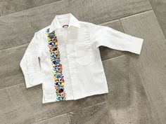 Beautiful Mexican White with Multicolor Embroidered Guayabera Long or Short Sleeve / Polycotton Different sizes Size 6 months to 16 years LS stands for Long Sleeve SS stands for Short Sleeve This is a matching Adult/Boy Guayabera https://www.etsy.com/listing/1262188464/classic-guayabera-white-and-colorful?click_key=57508c80a5f75c4ab3a5e667b079bf645d42cb05%3A1262188464&click_sum=30cd7082&ref=shop_home_active_2&frs=1&sts=1 THIS SHIRT RUNS SMALL, please check measurements , you can find them between pictures.  Please check measurements before to place the order. Mexican Shirts, Collarless Shirt, Mexican Outfit, Boys Tops, Mexican Dresses, Boys Top, Embroidered Shirt, Boys Shirts, Boy Shorts