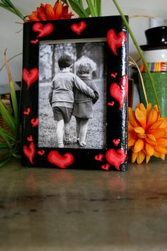 a black frame with red hearts on it next to an orange flower and potted plant