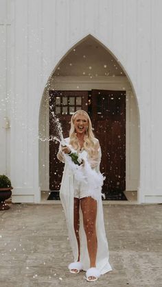 a woman standing in front of a white building with snow falling on her and holding a bouquet