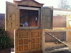 an outdoor chicken coop made out of wood and metal wire, with the doors open