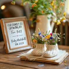 two knitted baby booties sitting on top of a wooden table next to a vase with flowers