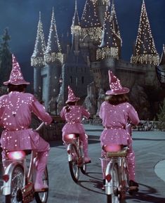 three people in pink outfits riding bikes with lights on them and castle in the background