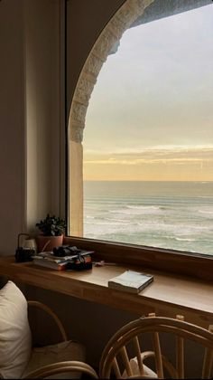 an arched window overlooks the ocean from a room with a desk and chair in front of it