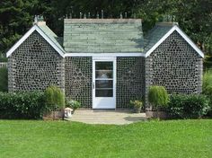 a small house made out of bottles in the middle of some grass with trees and bushes around it