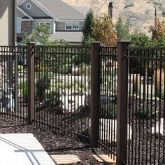 an iron fence in front of a house with cars parked on the street behind it