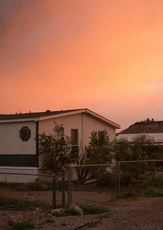 the sky is pink and orange as the sun sets over a small building with a clock on it