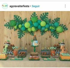 a table topped with lots of desserts covered in green balloons and jungle animals on top of it