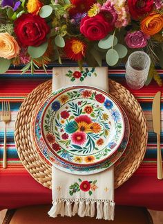 a colorful table setting with flowers and place settings on the plates, napkins and forks