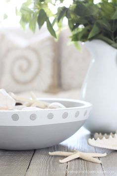 a white bowl sitting on top of a wooden table next to a vase filled with flowers