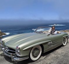 a man sitting in the driver's seat of an old fashioned car near the ocean