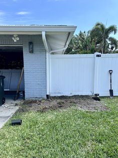 a house with a white fence and green grass in front of it, next to a black trash can