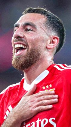 a close up of a person with a beard and wearing a red shirt smiling at the camera