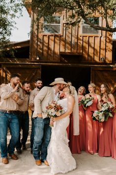 a bride and groom kissing with their bridal party in front of a rustic barn