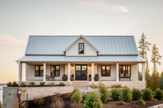 a white house with a metal roof and two porches on the front, surrounded by greenery