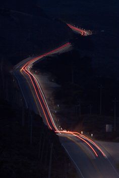 an aerial view of a highway at night with light streaks on the road and trees in the background