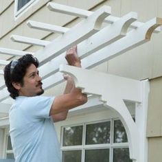 a man is holding up a white trellis on the side of a house,