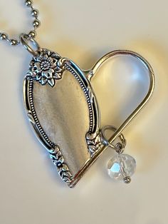 a silver heart shaped locke with a crystal bead hanging from it's side