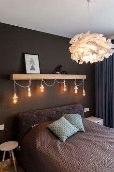 a bed sitting in a bedroom next to a window with lights hanging from the ceiling