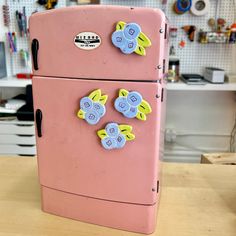 a pink refrigerator with magnets on it sitting on a table in a room filled with craft supplies