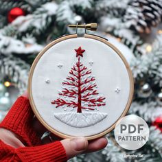 a hand embroidered christmas tree ornament in front of a decorated christmas tree with red and white ornaments