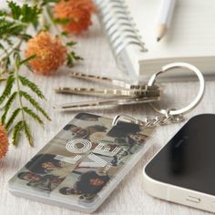 a cell phone with a keychain attached to it sitting next to some flowers