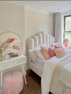 a white bed sitting next to a window with pink pillows and blankets on top of it