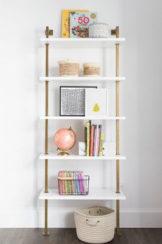 a white book shelf with books and baskets on it in front of a white wall