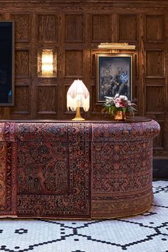 a table with a lamp on top of it in front of wooden paneled walls