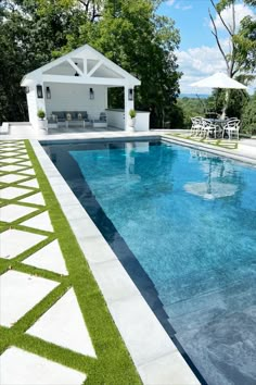 an outdoor pool with grass on the ground and lawn chairs around it, in front of a white gazebo