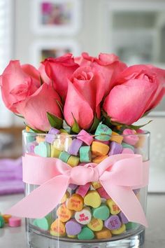 pink roses are in a glass vase filled with candy and marshmallow candies