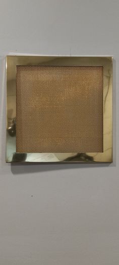 a close up of a metal object on a white wall with a gold colored frame