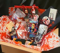 an open box filled with halloween items on top of a black surface and red splattered paper