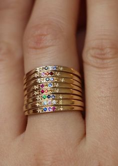 a woman's hand with five gold rings on top of each other and four different colored stones in the middle