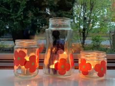 three jars filled with candles sitting on top of a counter next to a window sill