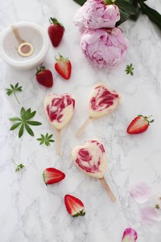 strawberries and flowers on a marble surface with popsicles shaped like heart shapes