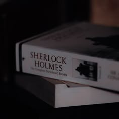 two books sitting on top of each other in front of a black background with the words sherlock holmes