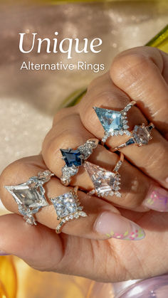 a woman's hand holding five rings with blue and white diamonds on them, all in different shapes and sizes