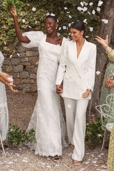 two women in white dresses and one is holding her hand out as she walks down the aisle