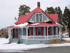 a small blue house with red roof and white trim on the front porch is covered in snow