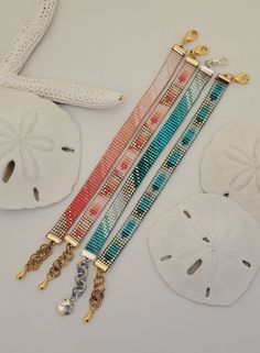 three bracelets with charms and shells on a white table next to starfish, sand dollar