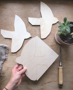 someone is making wooden birds out of plywood on a table next to a potted plant