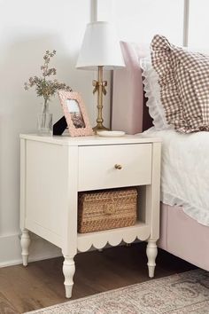 a white nightstand with a basket on it next to a bed