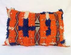 an orange and blue pillow with fringes on it's sides, sitting on a white surface