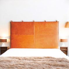 a bed with two lamps on either side and a brown leather headboard above it