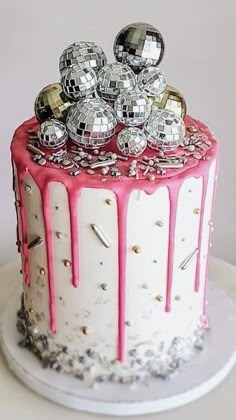 a white cake with pink icing and disco balls on top is sitting on a plate