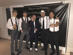 four men in suits and ties are posing for a photo with one holding a beer