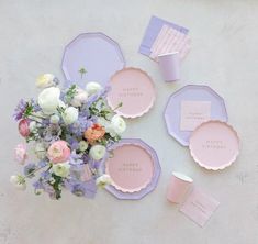 the table is set with pastel pink and purple plates, napkins, and flowers