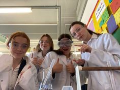 four girls in lab coats and goggles giving thumbs up while holding beaks filled with liquid