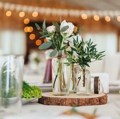 three vases filled with flowers on top of a wooden slab at a wedding reception