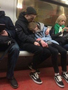 three people sitting on a subway bench with their arms around each other and looking at their phones